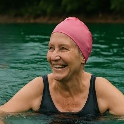 An older woman im a swim cap, smiling as she enjoys being in the open water
